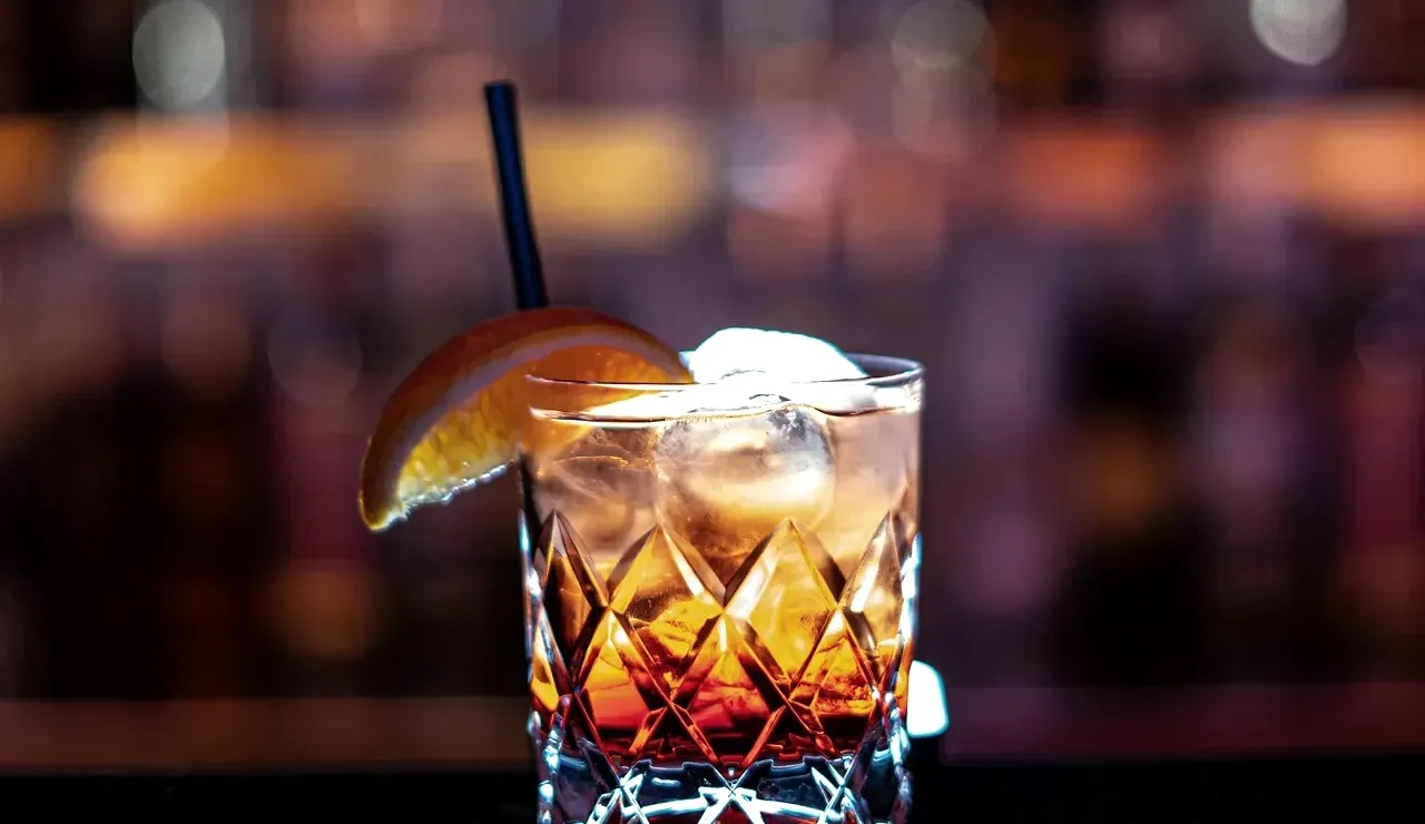 Old Fashioned-style cocktail with ice and an orange slice on a dark bar top