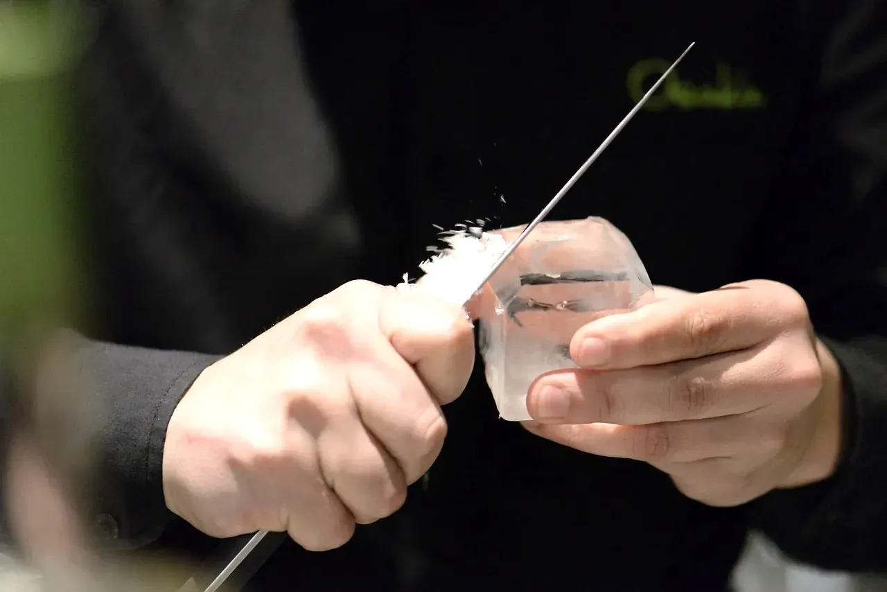 Hands carving a block of clear ice for a cocktail