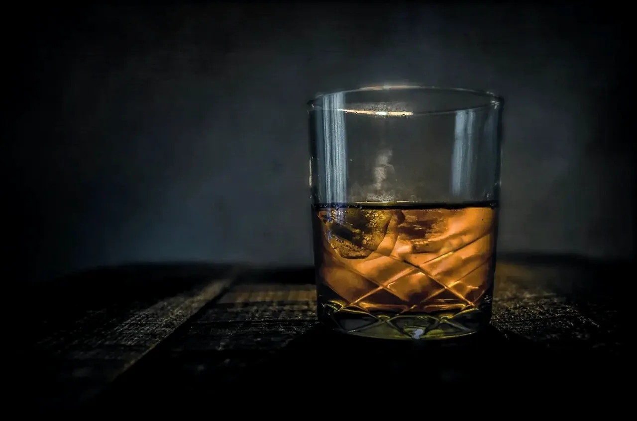 A glass of whiskey on ice on a dark wooden table